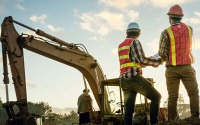 Workers standing with backhoe on job site